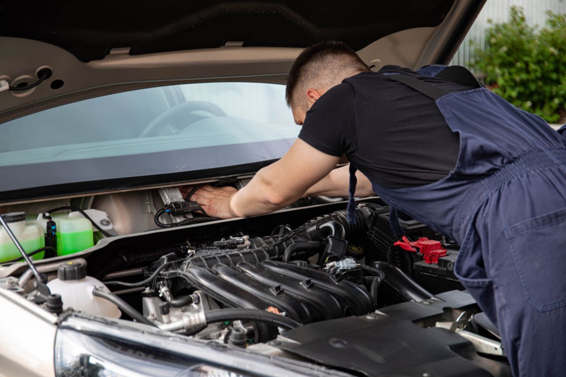 Technician working at an open engine bay beside the coolant reservoir and intake manifold