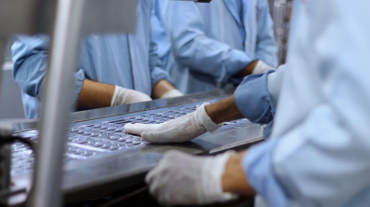 Operators in clean-room coats inspecting components on a production tray